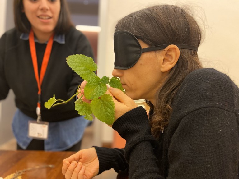 Una partecipante al laboratorio, bendata, annusa e sfiora un campione botanico