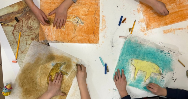 Foto con dettaglio di mani di bambini che colorano alcuni disegni